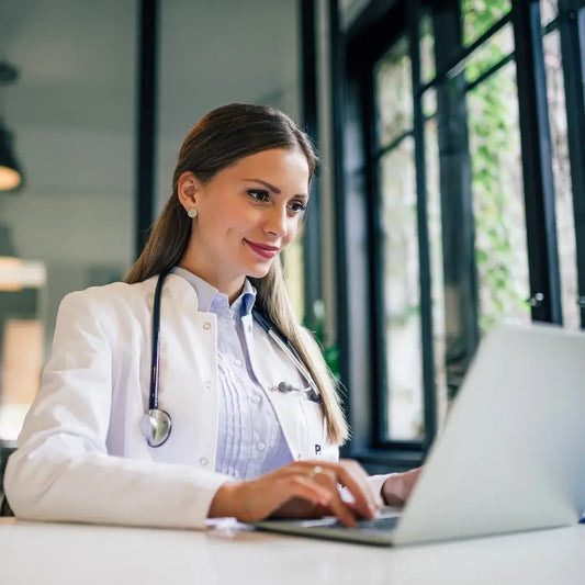 Smiling female doctor seated at a computer, confidently engaged in her work."